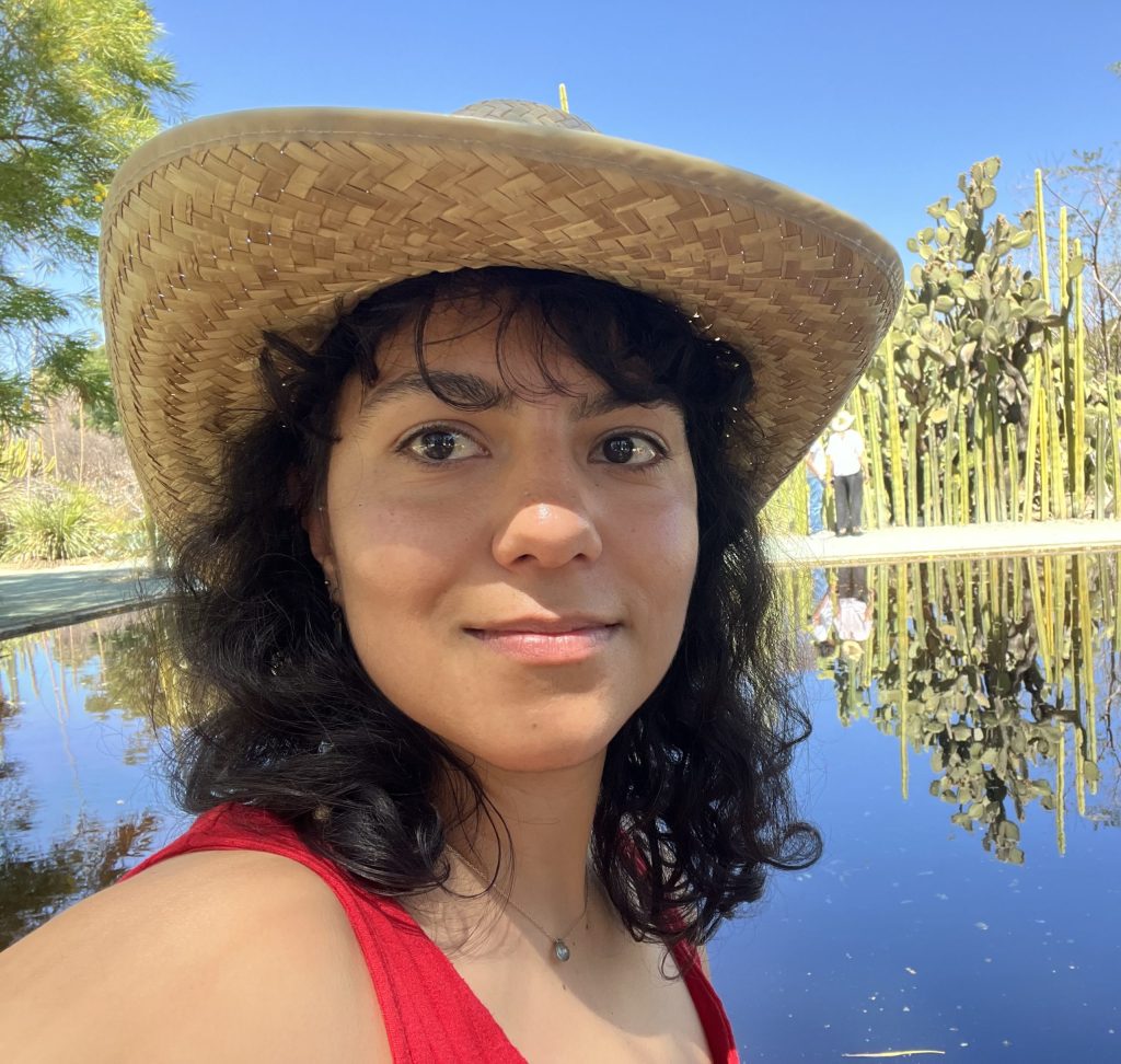 A woman smiles into the camera while wearing a hat