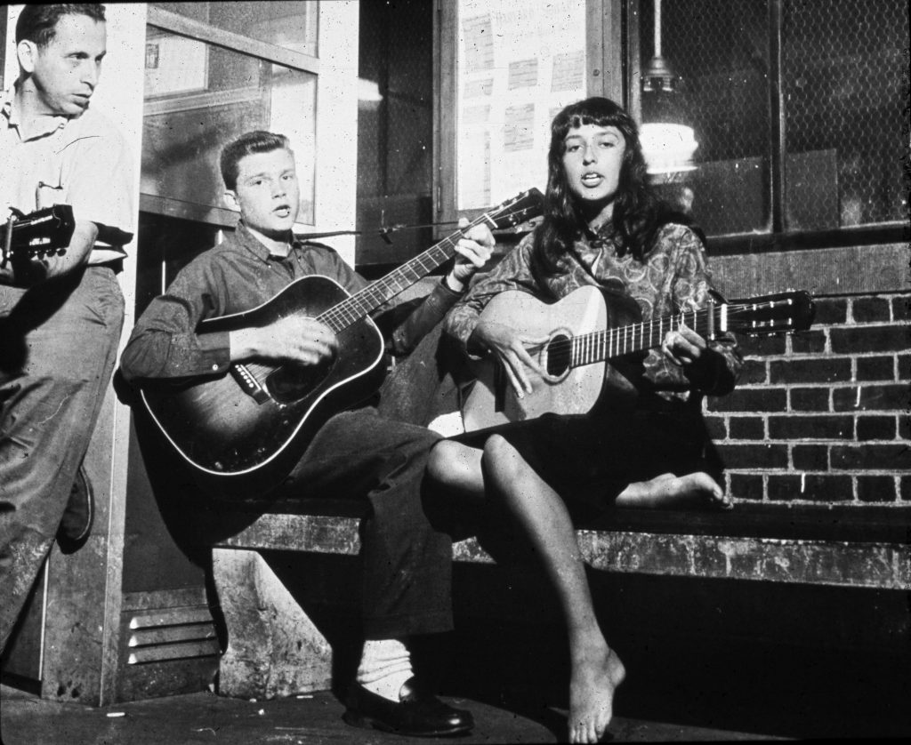 Ted Alevisos and Bill Wood accompany Joan Baez behind the kiosk, 1959.