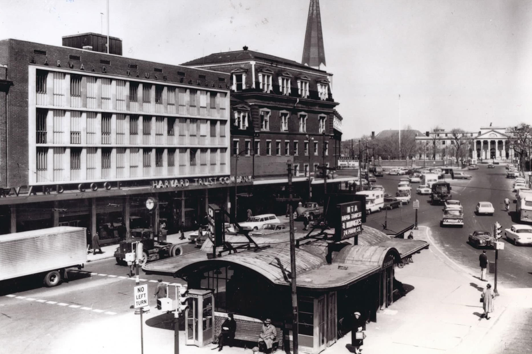 A view of harvard square taken in 1979 shows the kiosk with cars on either side and people sitting in front of it.