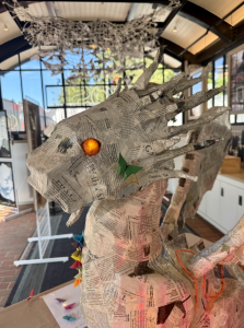 headshot of a papier-mâché dragon with glowing yellow eyes
