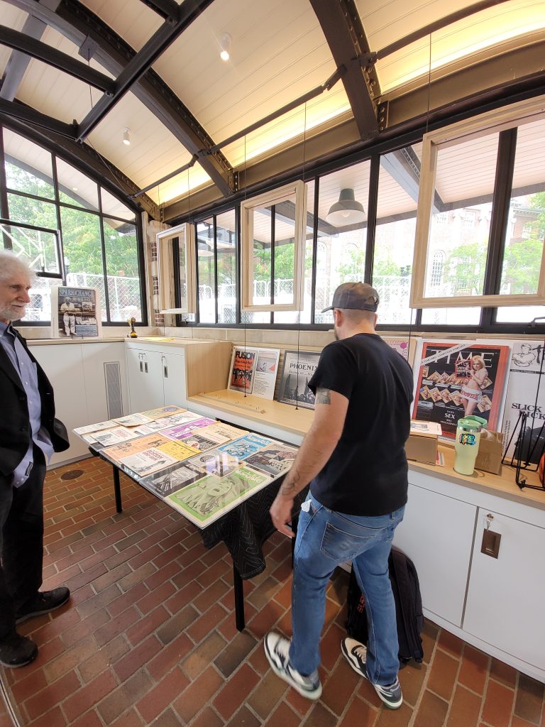 Chris Faraone and David Bieber cover a table wioth colorful front pages from old newspapers as part of the Cambridge: Then and Now exhibition