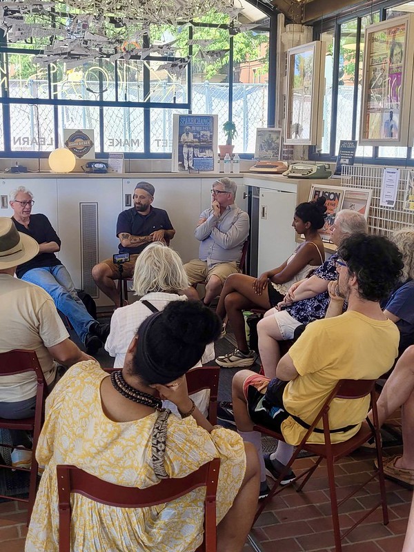 Visitors at the KiOSK sit on red chairs while listening to a speaker talk.