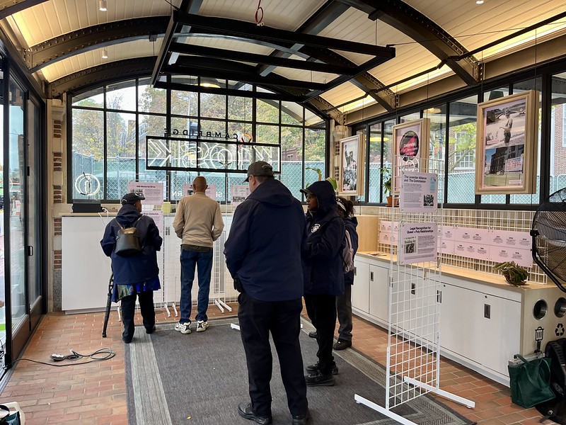 Visitors read pink signs from the Queer History Boston exhibition at the KiOSK.