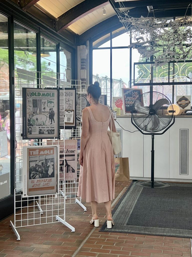 A visitor in a pink dress looks at framed newspaper front pages on display as part of the Cambridge: Then and Now exhibition