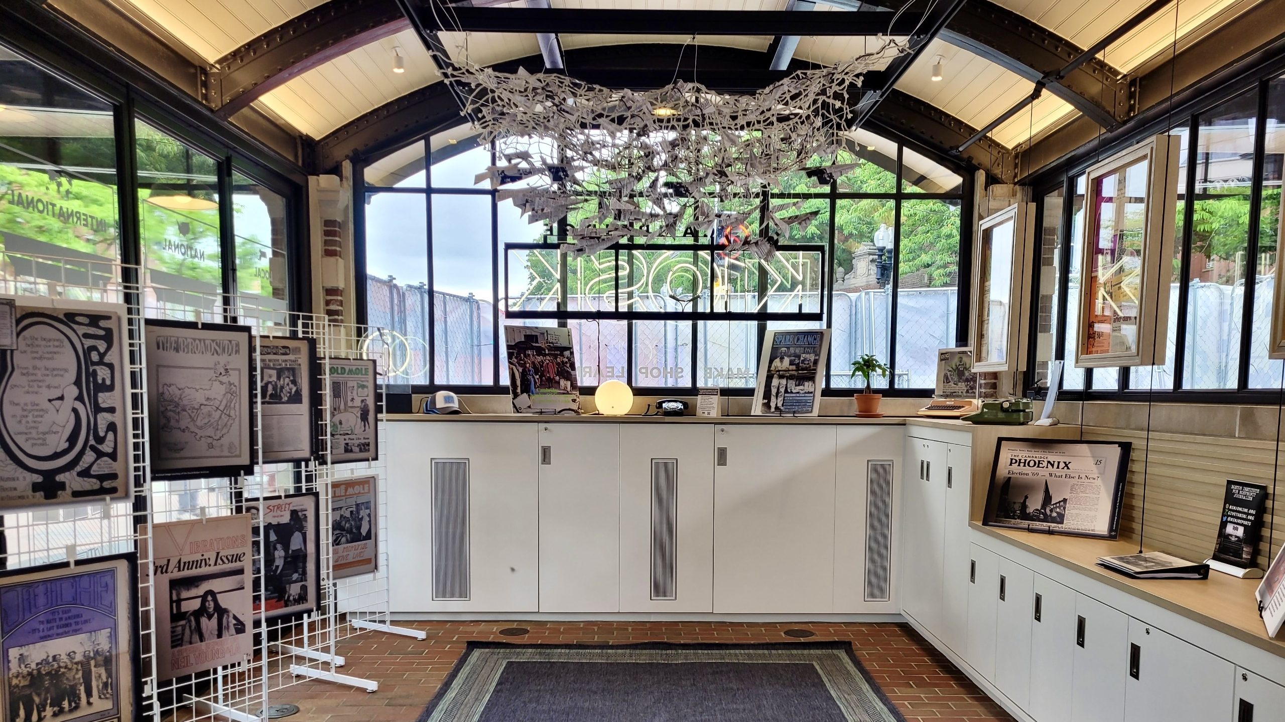 Framed archival newsprint and and an installation of hanging paper planes display at the KiOSK.
